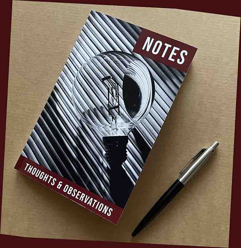 A high-angle, close-up shot captures a lined notebook with a sleek black pen resting diagonally.